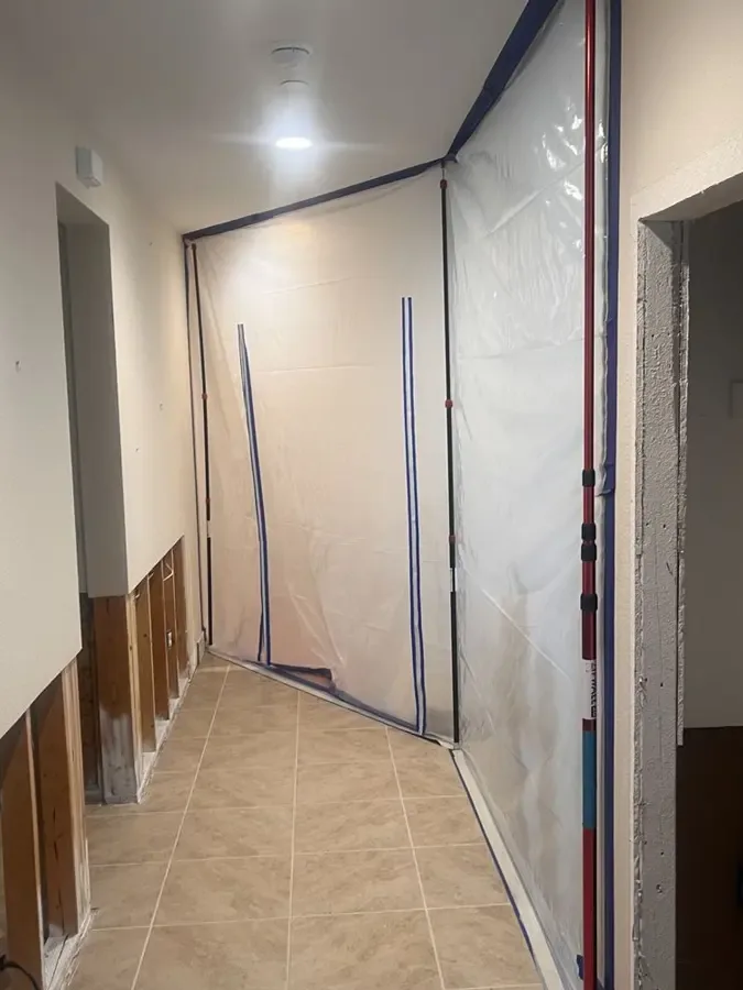 Lower drywall removed along a hallway with plastic containment around a doorway